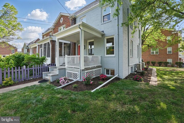 view of front of house with brick siding, a front lawn, fence, and covered porch