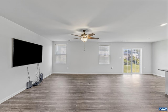 unfurnished living room featuring baseboards, a ceiling fan, wood finished floors, and a healthy amount of sunlight