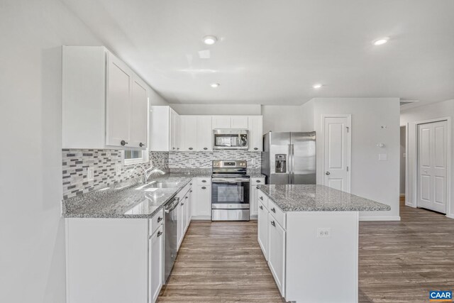 kitchen with decorative backsplash, a center island, a sink, light stone counters, and stainless steel appliances