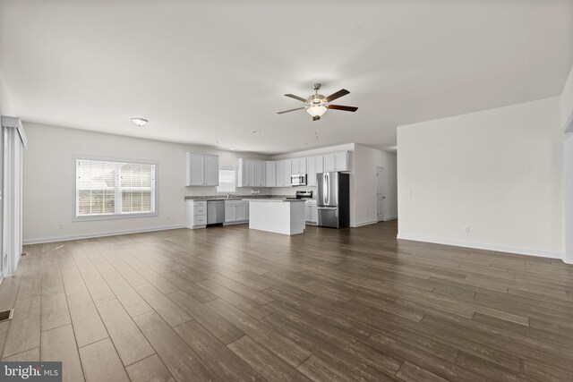 unfurnished living room featuring a ceiling fan, baseboards, dark wood finished floors, and a sink