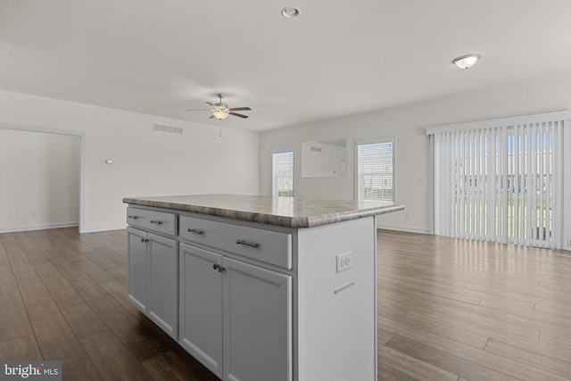 kitchen featuring visible vents, a kitchen island, open floor plan, ceiling fan, and dark wood-style floors
