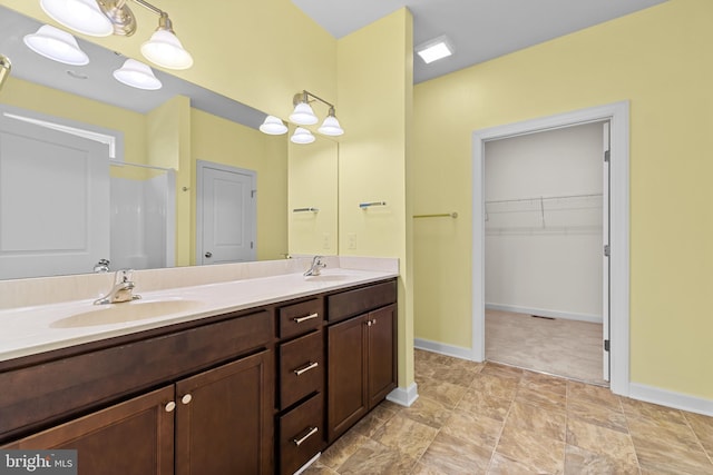 bathroom with double vanity, baseboards, a sink, and a walk in closet