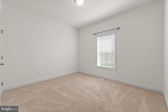 spare room featuring baseboards, visible vents, and light carpet