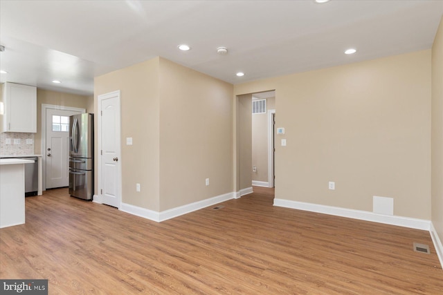 unfurnished living room with visible vents, light wood finished floors, and baseboards