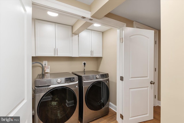 washroom featuring light wood-style floors, baseboards, cabinet space, and washing machine and clothes dryer