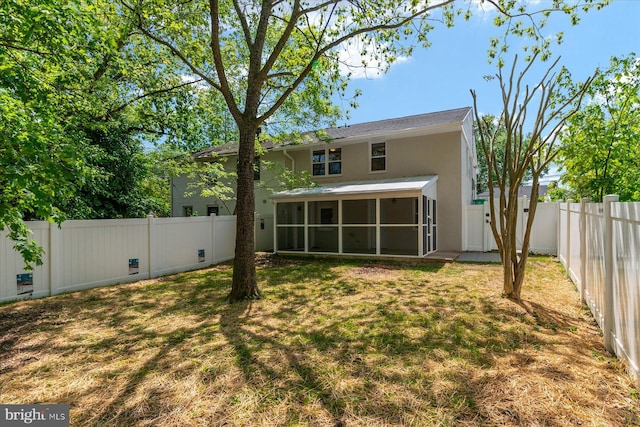 back of house featuring a yard, a fenced backyard, a sunroom, and stucco siding