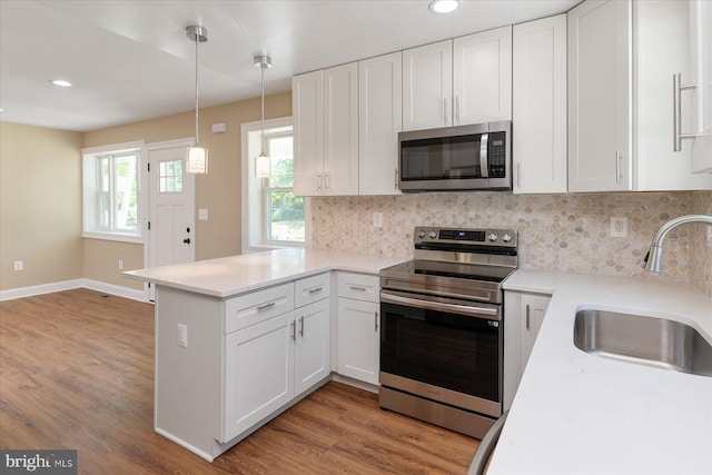 kitchen with decorative backsplash, appliances with stainless steel finishes, a sink, white cabinets, and a peninsula