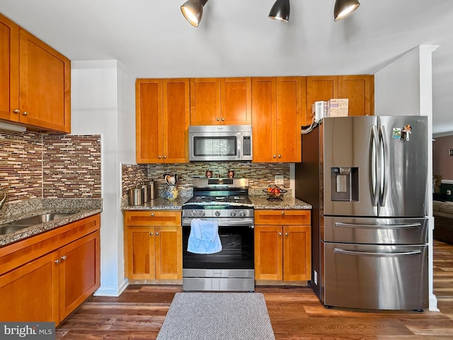 kitchen featuring dark stone counters, backsplash, stainless steel appliances, and dark wood-type flooring