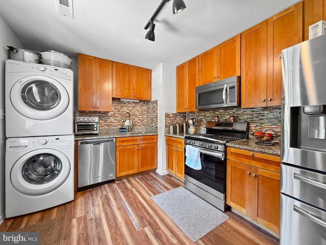 kitchen featuring visible vents, appliances with stainless steel finishes, stacked washing maching and dryer, a sink, and light wood finished floors