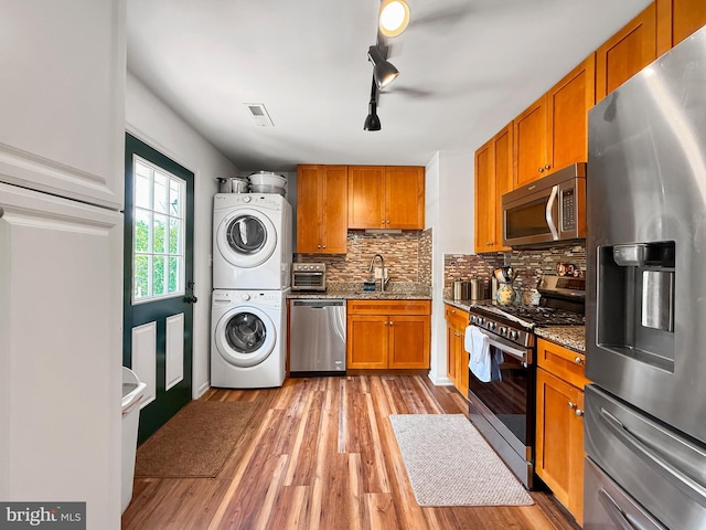 kitchen with stacked washer / drying machine, a sink, light wood finished floors, stainless steel appliances, and decorative backsplash