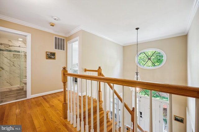 hallway with light wood-style flooring, baseboards, an upstairs landing, visible vents, and ornamental molding