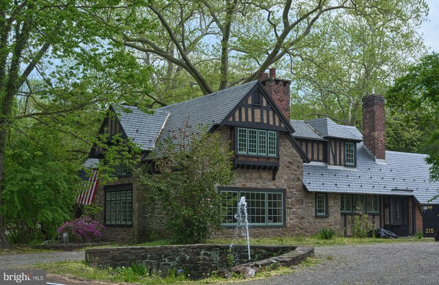 view of home's exterior with stone siding, a chimney, and a high end roof