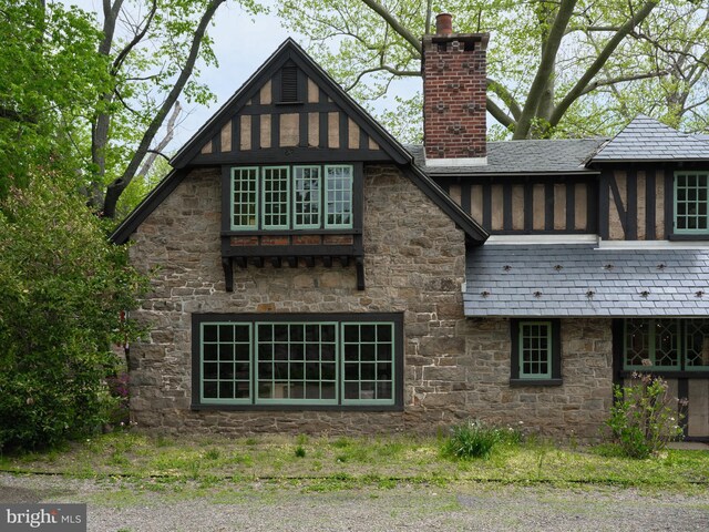 rear view of property featuring stone siding, a chimney, and a high end roof