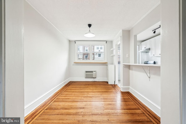 unfurnished dining area featuring a wall unit AC, light wood-style flooring, and baseboards