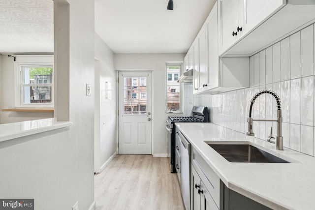 kitchen with a sink, under cabinet range hood, appliances with stainless steel finishes, light wood-style floors, and light stone counters