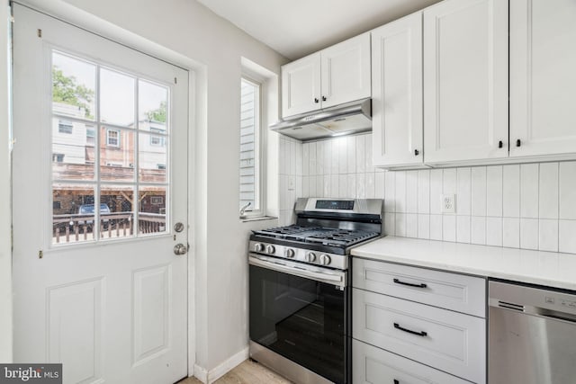 kitchen featuring stainless steel appliances, under cabinet range hood, decorative backsplash, and white cabinetry
