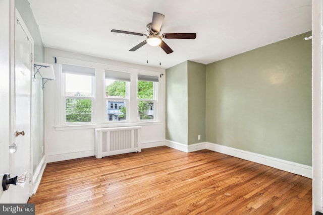 spare room with radiator, light wood-style floors, ceiling fan, and baseboards