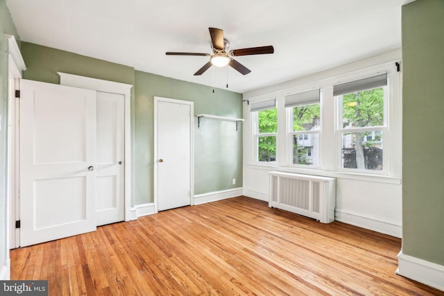 unfurnished bedroom with radiator, light wood-type flooring, baseboards, and two closets