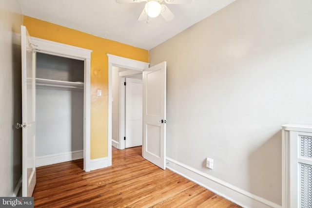 unfurnished bedroom featuring wood finished floors, a closet, baseboards, and ceiling fan