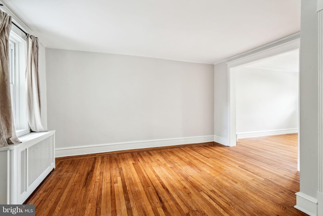 empty room with radiator, wood-type flooring, baseboards, and crown molding