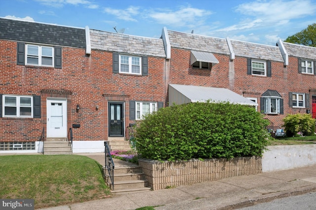 view of property featuring brick siding, mansard roof, a high end roof, and entry steps
