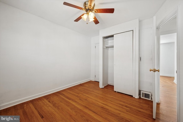 unfurnished bedroom with visible vents, a closet, wood finished floors, baseboards, and a ceiling fan