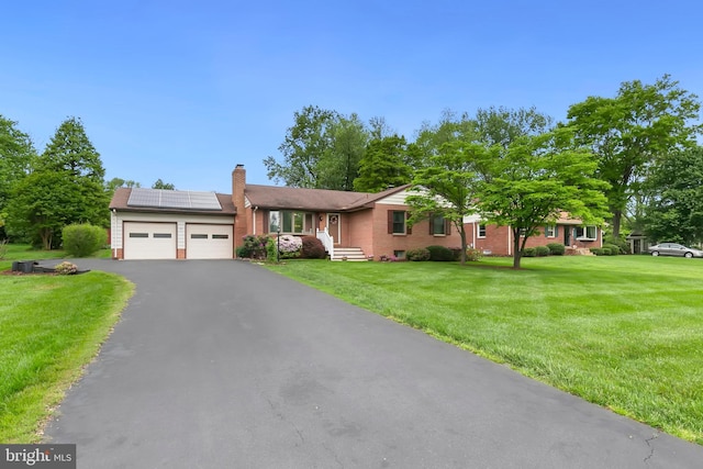 single story home featuring a chimney, driveway, brick siding, a garage, and roof mounted solar panels