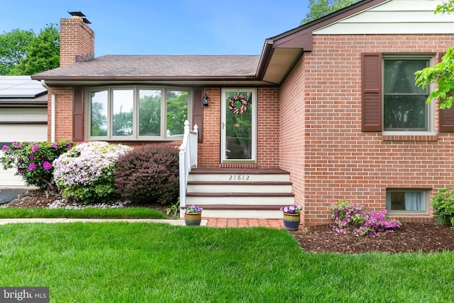 property entrance with a chimney, a yard, and brick siding