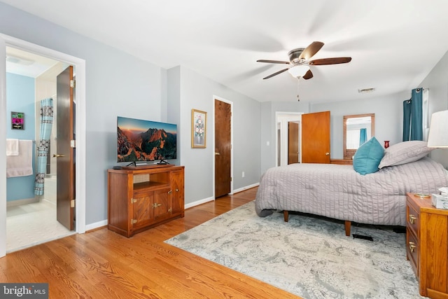 bedroom with connected bathroom, visible vents, wood finished floors, and baseboards