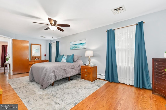 bedroom featuring a baseboard heating unit, ceiling fan, visible vents, and wood finished floors