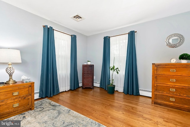 bedroom featuring a baseboard radiator, wood finished floors, visible vents, and multiple windows