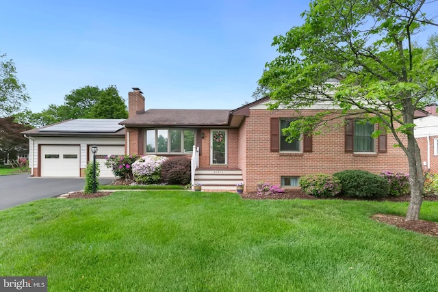 ranch-style home featuring a chimney, brick siding, solar panels, an attached garage, and aphalt driveway