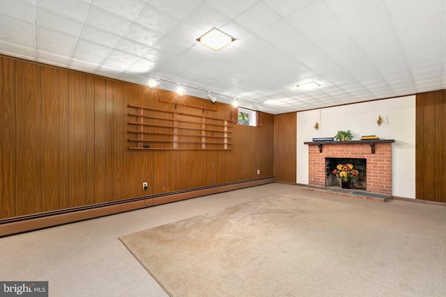 unfurnished living room with a baseboard heating unit, rail lighting, carpet, wooden walls, and a brick fireplace