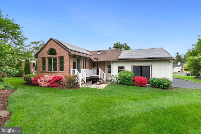 rear view of house with roof mounted solar panels, a chimney, a deck, a yard, and brick siding