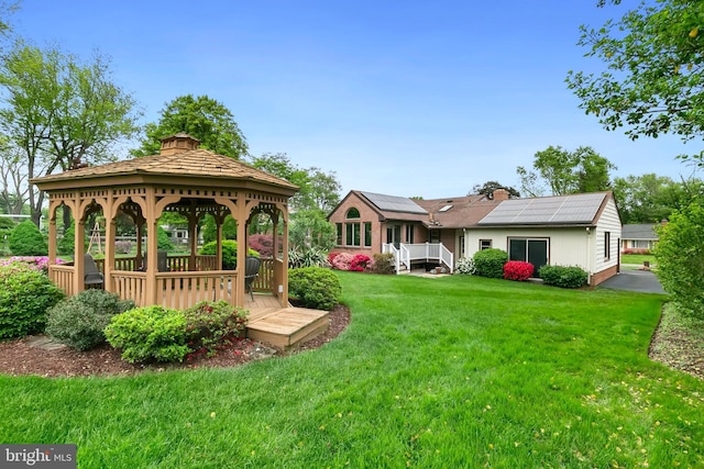 back of house with a chimney, a wooden deck, a lawn, solar panels, and a gazebo