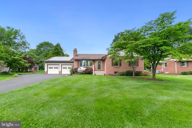 ranch-style house with roof mounted solar panels, a garage, a chimney, aphalt driveway, and brick siding