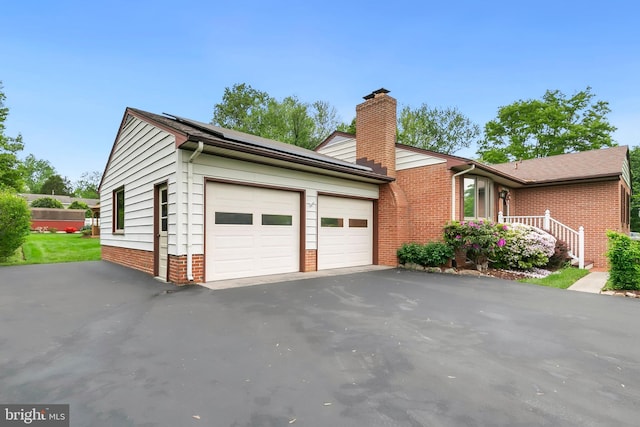 view of side of property featuring a garage, a chimney, brick siding, and driveway