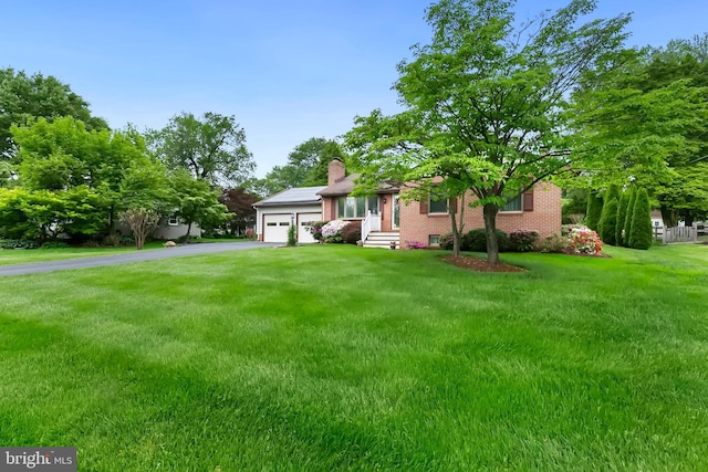 view of front of home featuring an attached garage, brick siding, driveway, a front lawn, and a chimney