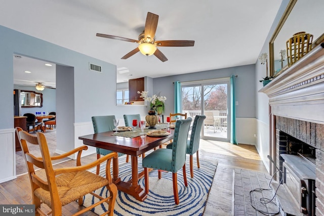 dining area featuring a ceiling fan, light wood-type flooring, visible vents, and wainscoting