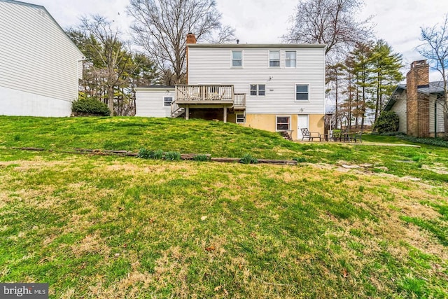 back of property with a wooden deck, a chimney, and a lawn