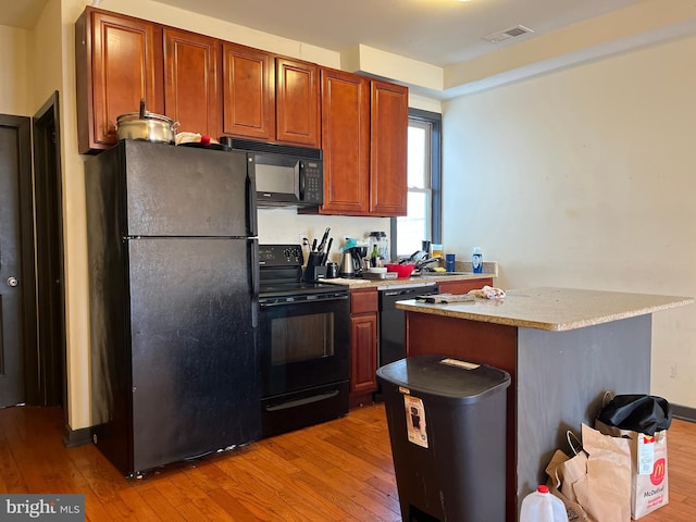 kitchen featuring visible vents, brown cabinetry, light wood-style floors, and black appliances