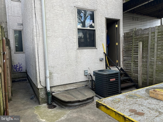 exterior details featuring stucco siding, central air condition unit, and fence