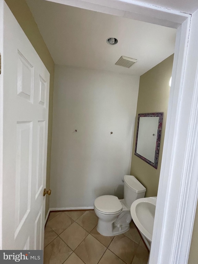 half bath featuring visible vents, a sink, tile patterned floors, baseboards, and toilet