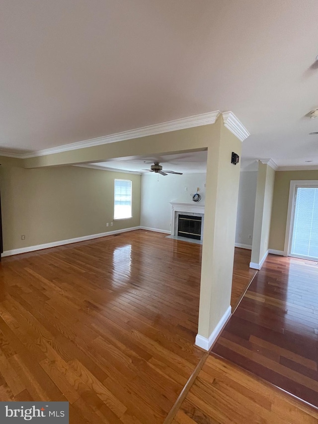 unfurnished living room featuring baseboards, a fireplace with flush hearth, ornamental molding, and wood finished floors
