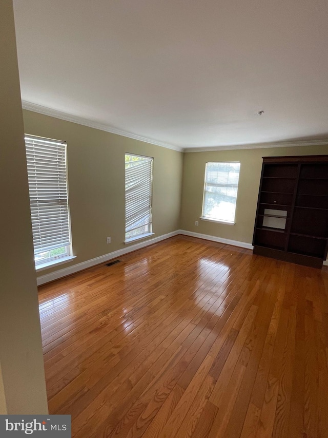 unfurnished room featuring crown molding, baseboards, hardwood / wood-style floors, and visible vents