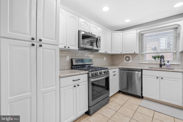 kitchen with decorative backsplash, light tile patterned flooring, white cabinets, a sink, and appliances with stainless steel finishes