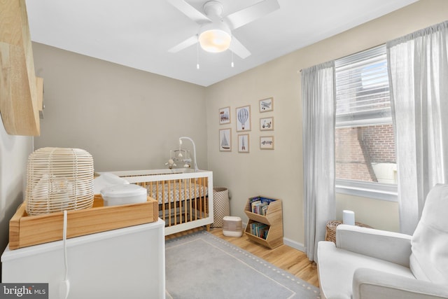 bedroom with baseboards, a ceiling fan, wood finished floors, and a nursery area