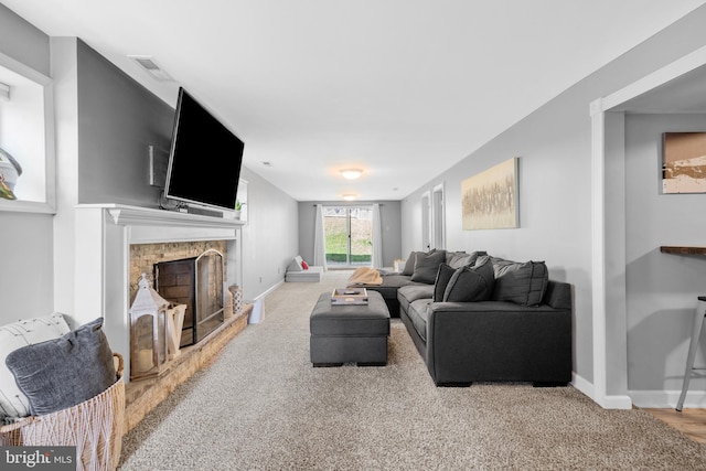 living area with visible vents, a fireplace with raised hearth, carpet, and baseboards