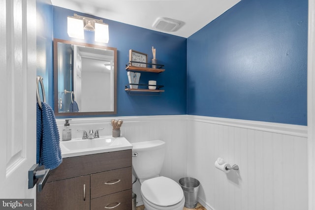 half bath with vanity, a wainscoted wall, visible vents, and toilet