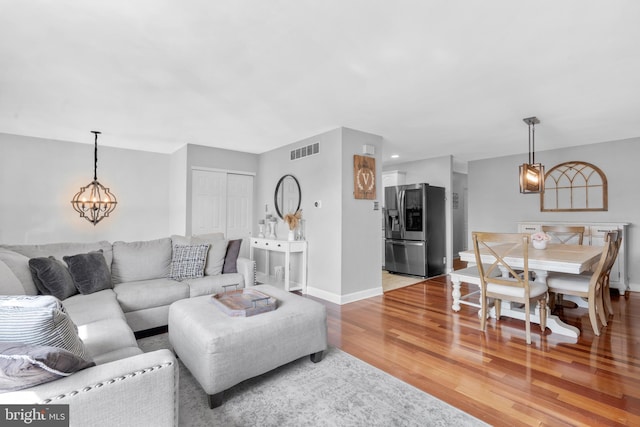 living area featuring baseboards, a notable chandelier, light wood-type flooring, and visible vents